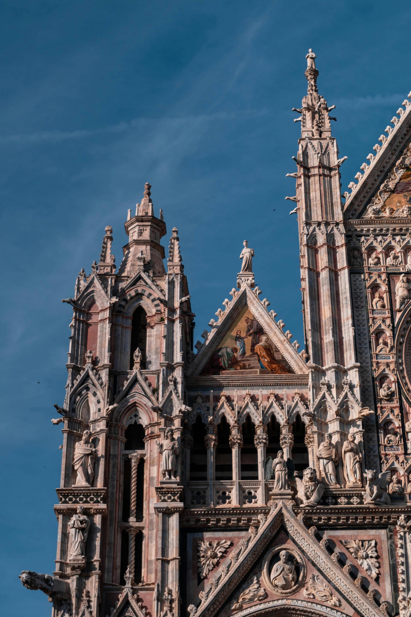 Close-up view of the ornate Gothic facade of Siena Cathedral under a clear blue sky.